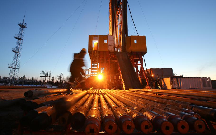 A worker passes an illuminated oil drilling rig, operated by Rosneft PJSC, in the Samotlor oilfield near Nizhnevartovsk, Russia, on March 21, 2017. 