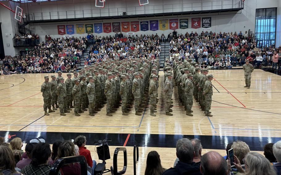 A group of soldiers stands in formation in a high school gym.