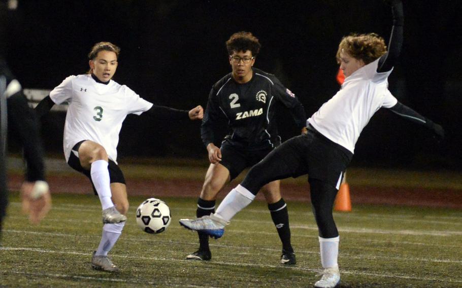 Robert D. Edgren’s Haruki Jones and Ethan Young and Zama’s Leon Phillips scuffle for the ball during Friday’s DODEA-Japan season-opening soccer match. The Trojans won 4-1.