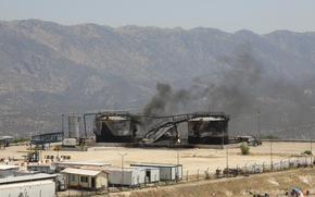 Smoke emerges from an oil field surrounded by mountains.
