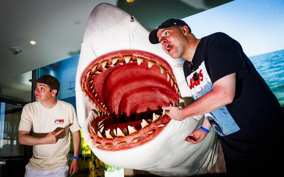 Two men pose for a photo next to a faux shark. 