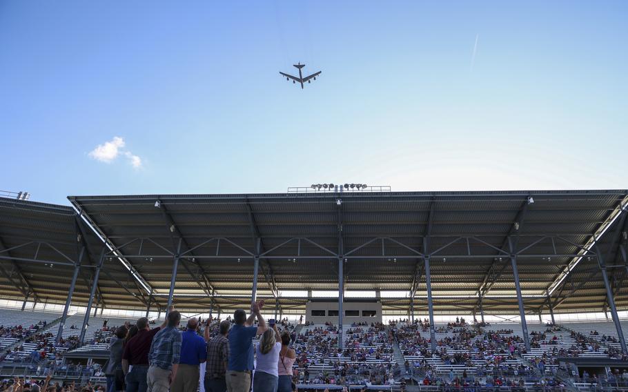 A B-52 bomber flies over bleachers filled with spectators.