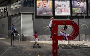 Children play on the letter "P" that is part of the acronym for the state-run oil company Petroleos de Venezuela S.A. (PDVSA) on the sidewalk in Caracas, Venezuela, Jan. 2, 2022. The United States government is moving to ease a few economic sanctions on Venezuela, which sits atop the world’s largest oil reserves and where about three quarters of its population live on less than $1.90 a day and lack access to clean, running water and electricity.