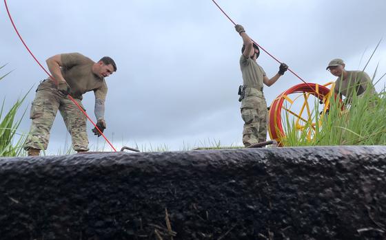 Air Force Staff Sgt. William Johnson, left, and cable antenna technicians Airman 1st Class Gabrielle Oropesa and Senior Airman Carlos Reye, feed a pull string into a duct rodder while replacing underground cable at Yokota Air Base, Japan, on Aug. 23, 2023. 