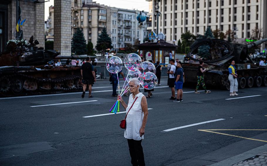 An elderly woman sells glowing balloons next to a destroyed Russian military equipment at Khreshchatyk street in Kyiv on Aug. 23, 2022, that was turned into an open-air military museum for a celebration of Ukraine’s Independence Day on Aug. 24, amid the Russian invasion of Ukraine. 