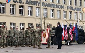 Col. Jorge Fonseca, the first commander of U.S. Army Garrison Poland, unfurls the unit’s colors during a ceremony March 21, 2023, in Poznan that was attended by high-level U.S. and Polish military officials.