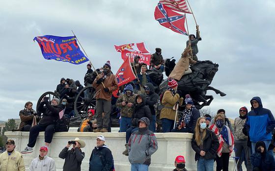 A man waving a Confederate flag and others watch rioters storm the Capitol in Washington, D.C., on Jan. 6, 2021. More than 100 of the 700 people accused so far of taking part in the assault on the Capitol served in the military, according to START, a national consortium for the study of terrorism.