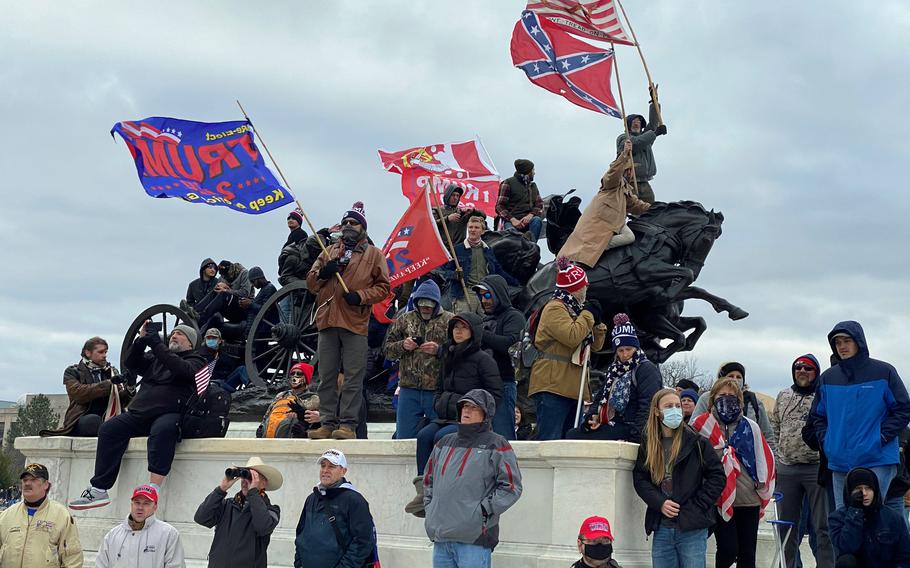A man waving a Confederate flag and others watch rioters storm the Capitol in Washington, D.C., on Jan. 6, 2021. More than 100 of the 700 people accused so far of taking part in the assault on the Capitol served in the military, according to a national consortium for the study of terrorism.