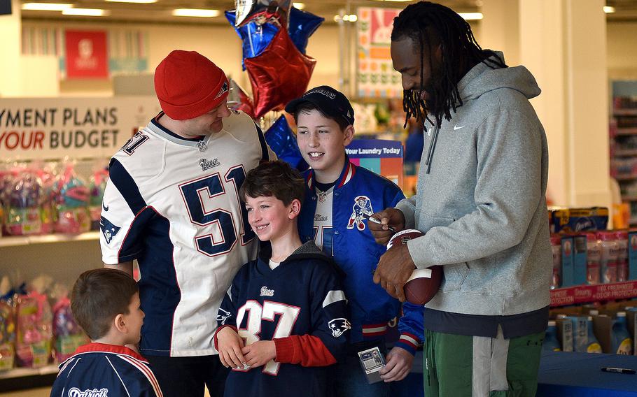 Chief Warran Officer3 Anthony Salame, left, and his sons, from left, Weston, 9, and Jaxon, 11, pose as New England Patriots outside linebacker Matthew Judon signs a football duirng an autograph event on March 23, 2024, at the Kaiserslautern Military Community Center on Ramstein Air Base, Germany. Logan Salame, 4, bottom left, watches Judon.