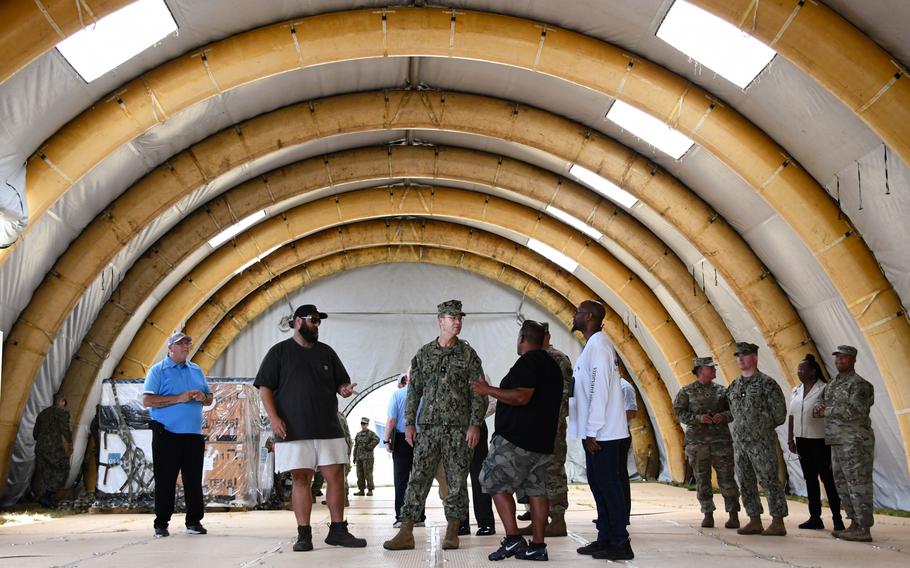 A group of people, some in uniform, stand underneath a temporary construction.