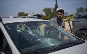 A man partially crouched emerging from or getting into a car seat, looking at the car’s cracked windshield.