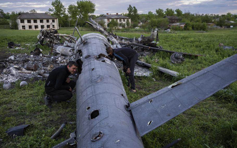 Oleksiy Polyakov, right, and Roman Voitko check the remains of a destroyed Russian helicopter lie in a field in the village of Malaya Rohan, Kharkiv region, Ukraine, Monday, May 16, 2022. 