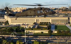 A military helicopter flies over a highway in front of the Pentagon filled with runners.