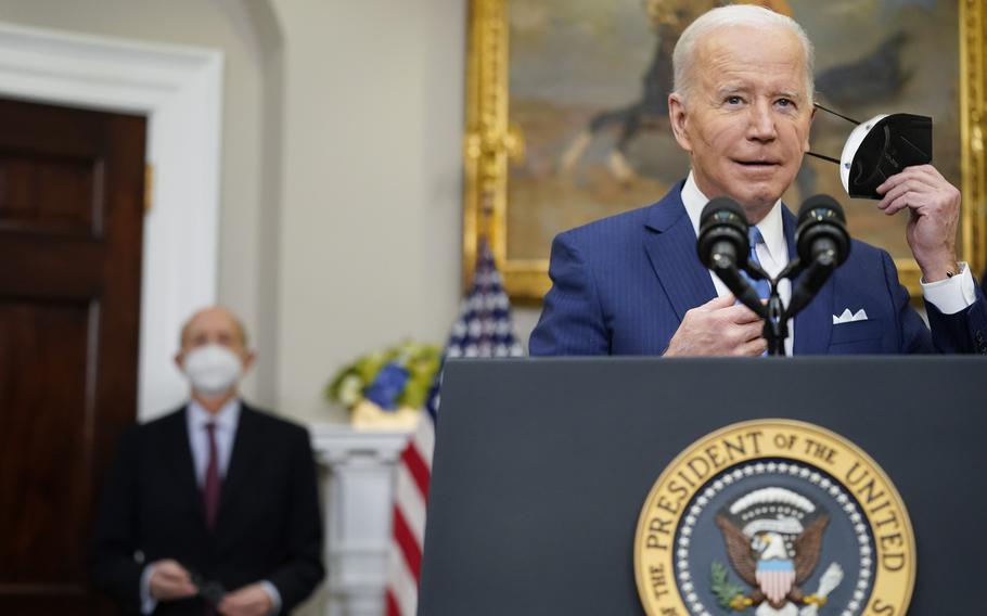 President Joe Biden removes his face mask as he prepares to deliver remarks on the retirement of Supreme Court Associate Justice Stephen Breyer, left, in the Roosevelt Room of the White House in Washington, Thursday, Jan. 27, 2022. 