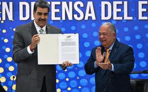Nicolas Maduro smiles while holding an official document in a folder, as another man next to him smiles and claps.