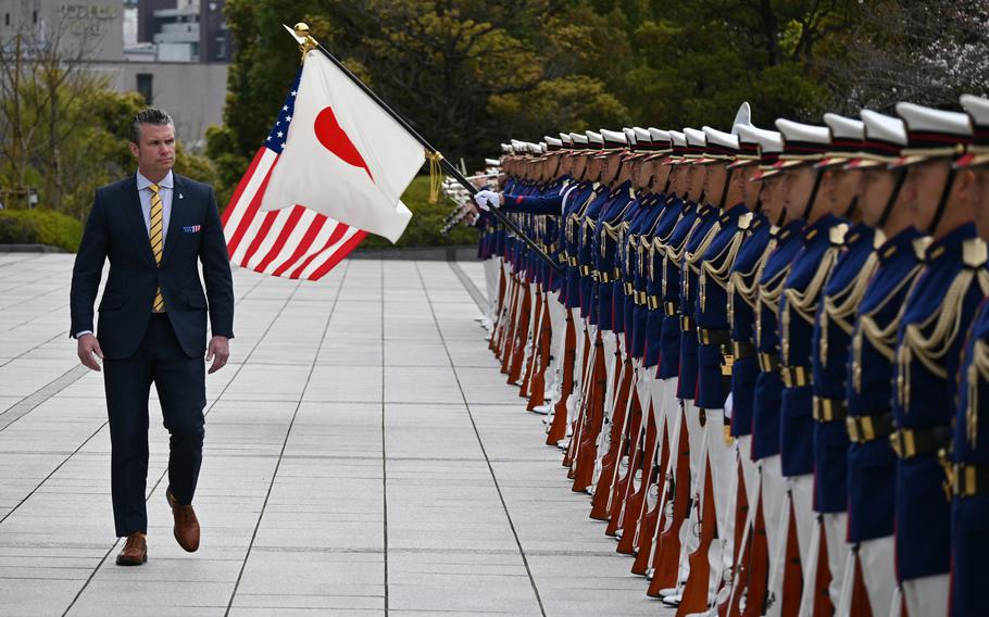 Pete Hegseth walks in front of a row of Japanese troops standing at attention in dress uniforms.