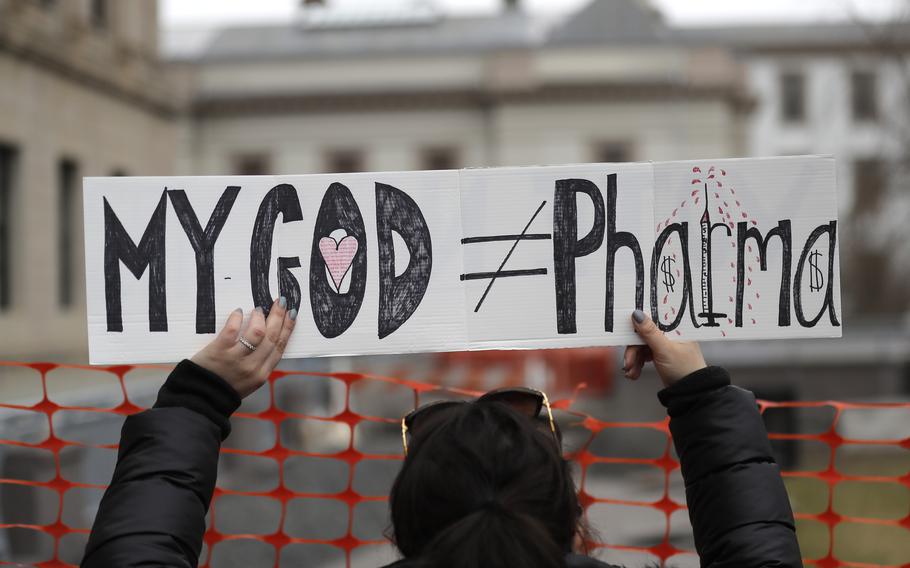 A woman holds a sign during a protest at the state house in Trenton, N.J., on Jan. 13, 2020. Religious objections are becoming a much more widely used loophole against the COVID-19 shot.