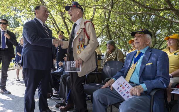 A man in a suit shakes hands with an elderly veteran.