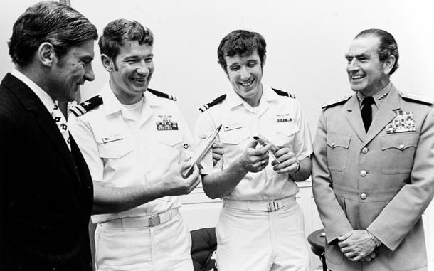 A black and white photo of four men smiling with one another, two of them in white uniforms.