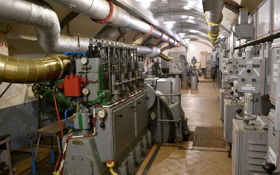 Long underground corridor with arched ceiling, containing mechanical equipment, pipes, and industrial machinery