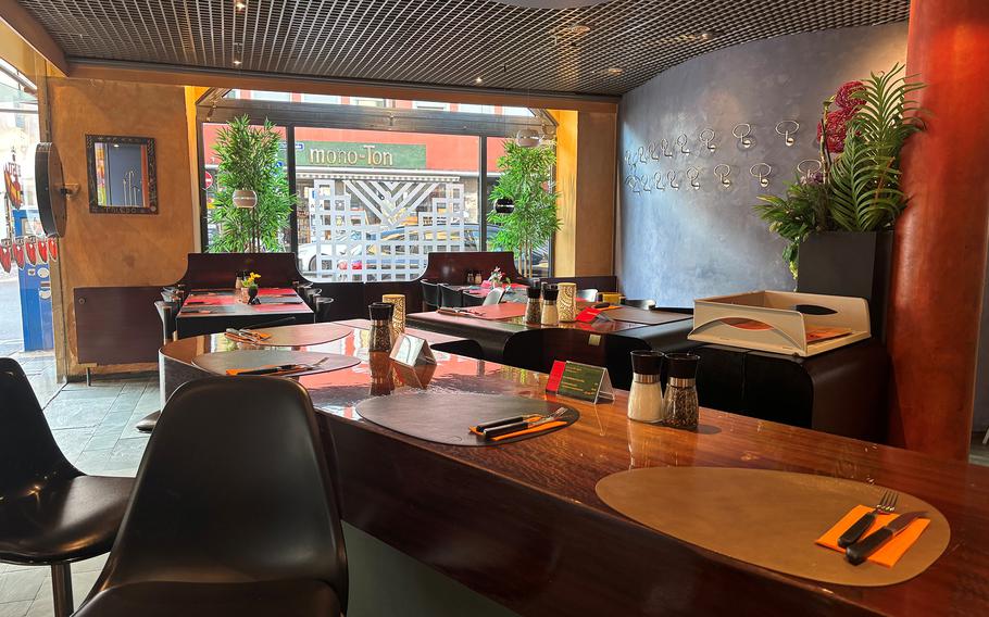 A long wooden bar with table settings and tables in the background.
