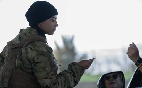A uniformed troop checks an ID card at the entrance to a military installation.