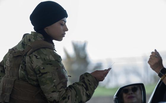 A uniformed troop checks an ID card at the entrance to a military installation.
