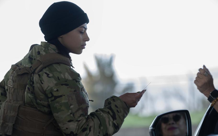 A uniformed service member checks an ID card at the entrance to a military installation.