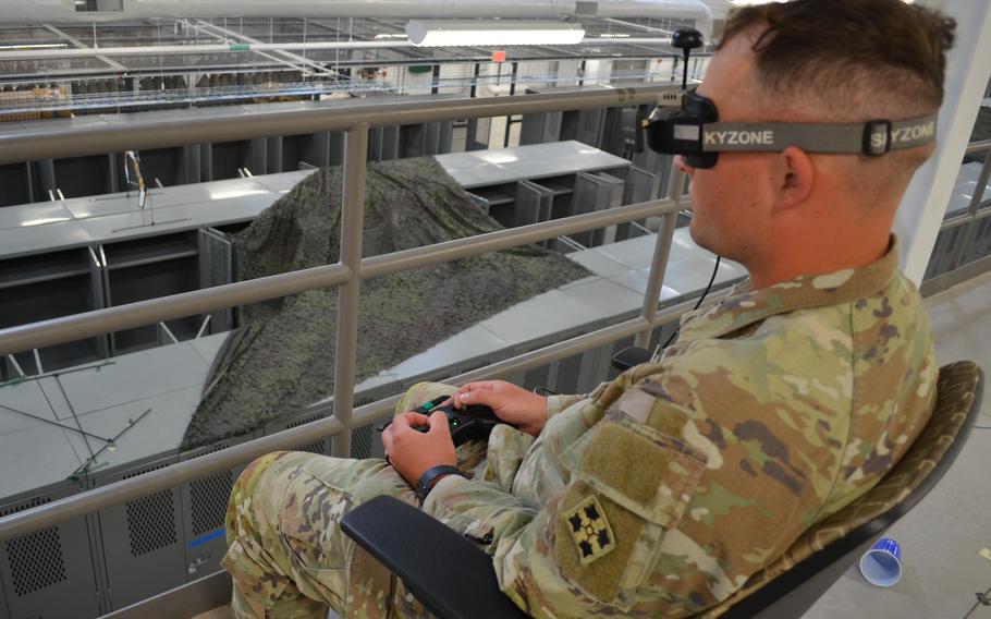 A soldier who is seated wears goggles and operates a remote control.