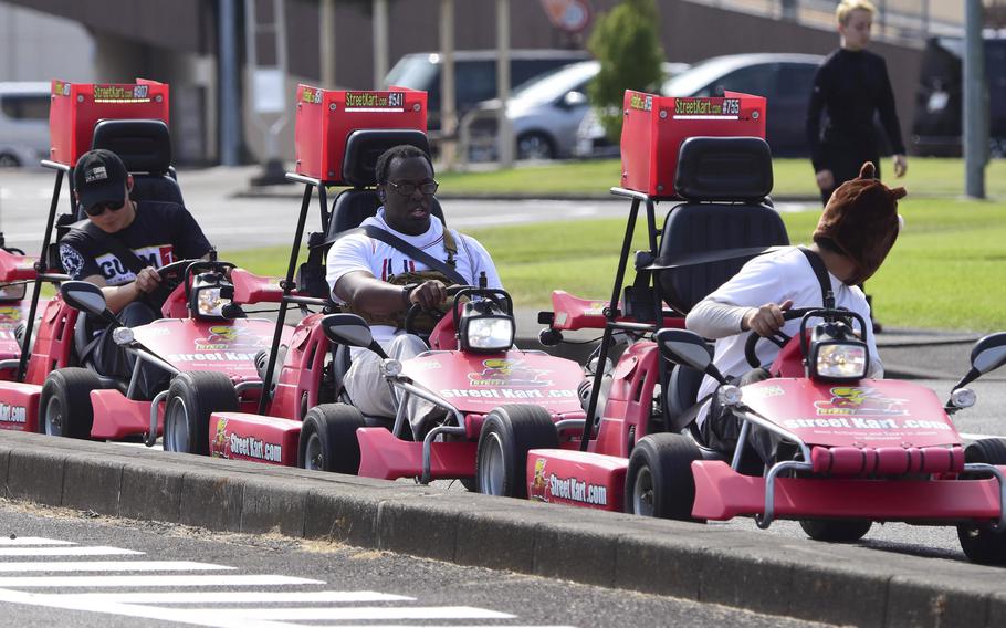 Three people sit in red go-karts in a line on an outdoor track.