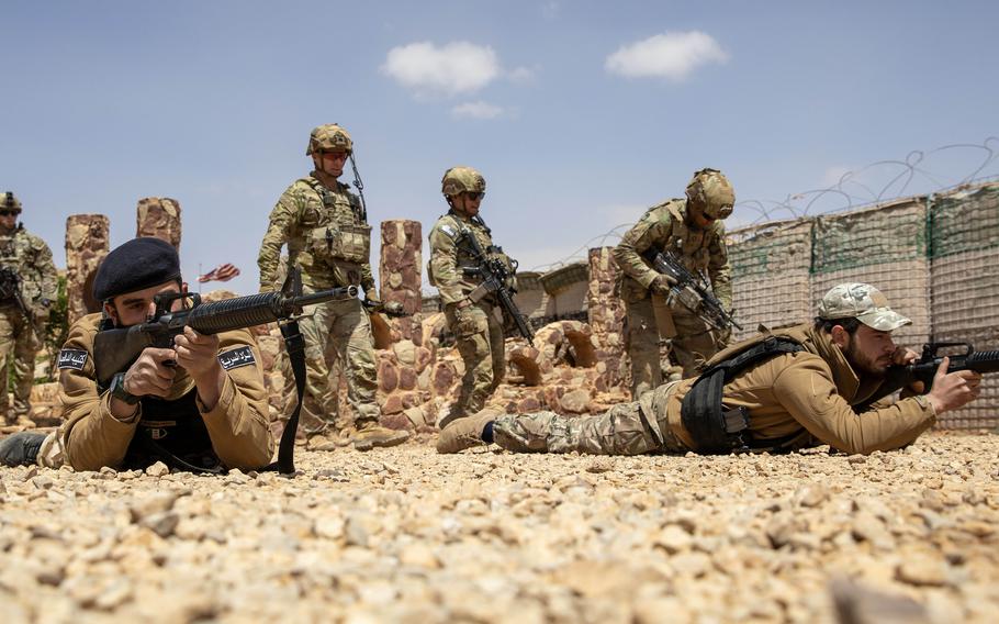 Syrian partner forces members lie on the ground with their weapons as U.S. soldiers look on.