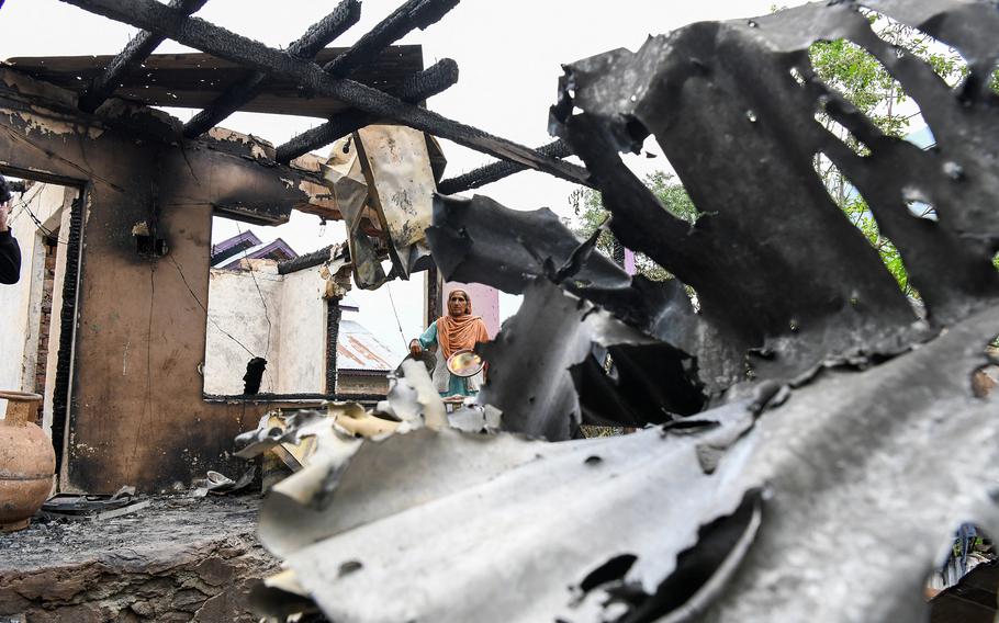 A woman stands in front of her damaged house