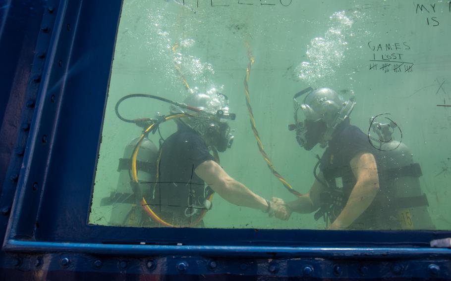 Two Navy divers shake hands underwater