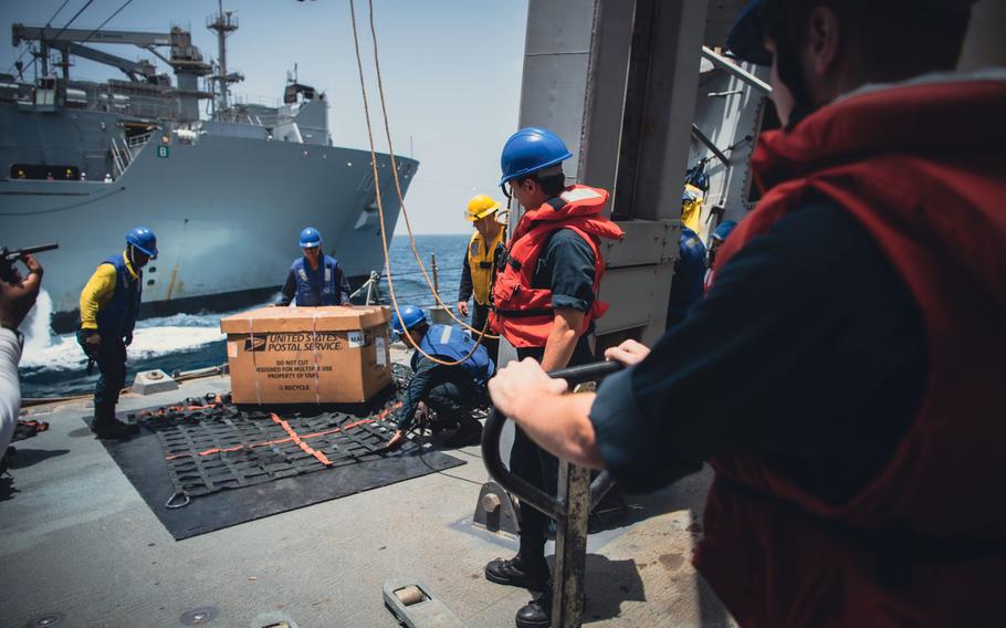 Sailors bring a box of mail on a ship.