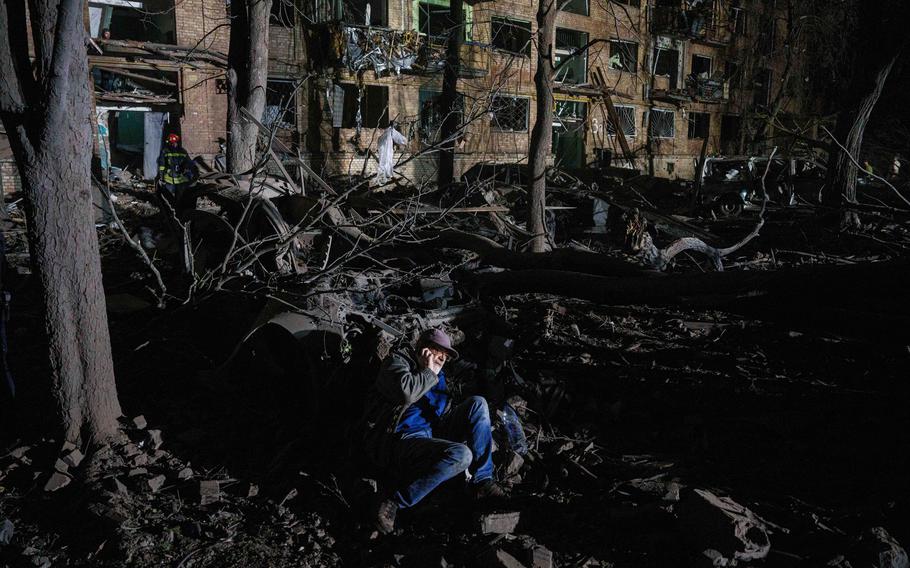 A man sits on the ground outside of a house damaged by a Russian airstrike.
