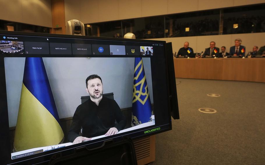 Volodymyr Zelenskyy seen on a TV monitor in the foreground as dignitaries are seen seated in the background.