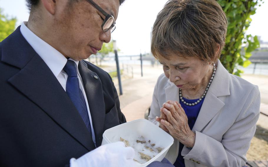 A woman holds her hands together while being shown human bone fragments in a box.