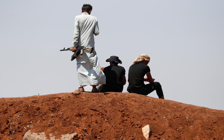 Armed fighters on hill, backs to the camera.