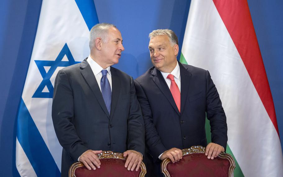 The leader of Israel and Hungary standing behind their chairs and looking at one another, in front of their respective flags.