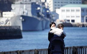 A mother wears a mask while holding her child near Yokosuka Naval Base, Japan, Tuesday, Jan. 18, 2022.