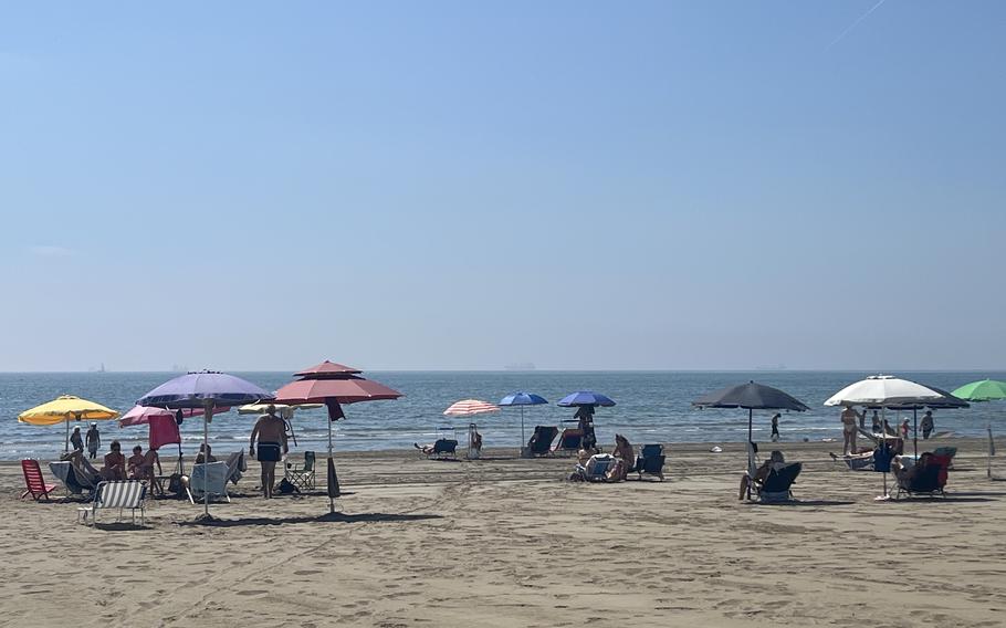 People sit on the beach beneath umbrellas.