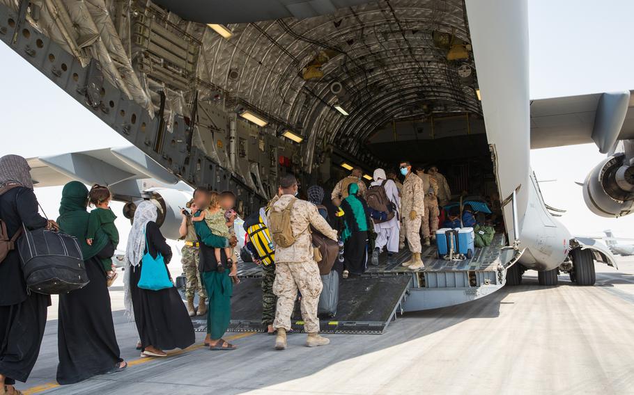 People boarding the back of a military aircraft with troops assisting them.