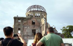 People take photos and read signs in front of the bombed wreckage of a domed building.