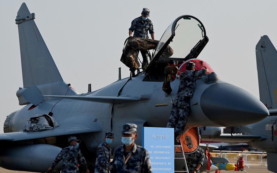 A fighter jet is seen with the pilot seat window open and military personnel clambering around it.