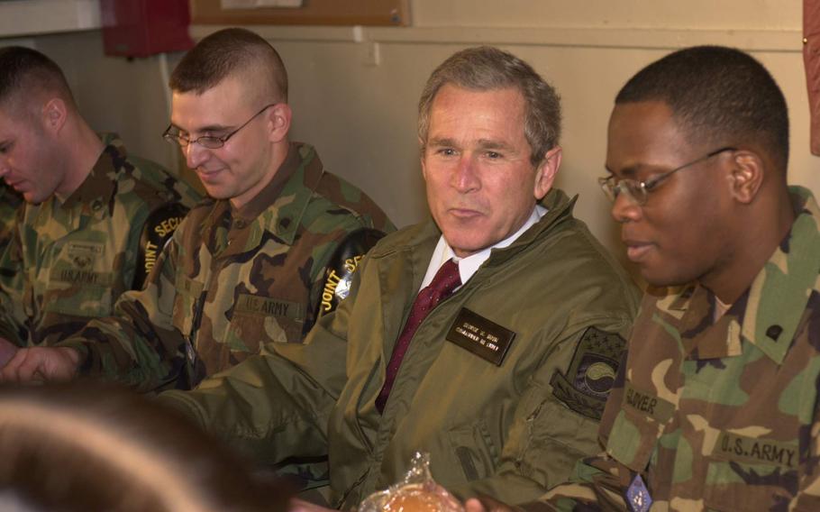 Then-President George Bush in the center-right of the photo while troops sit on either side of him.