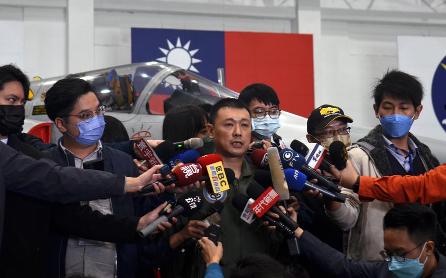 a pilot is surrounded by journalists holding microphones with the Taiwan flag visible in the background
