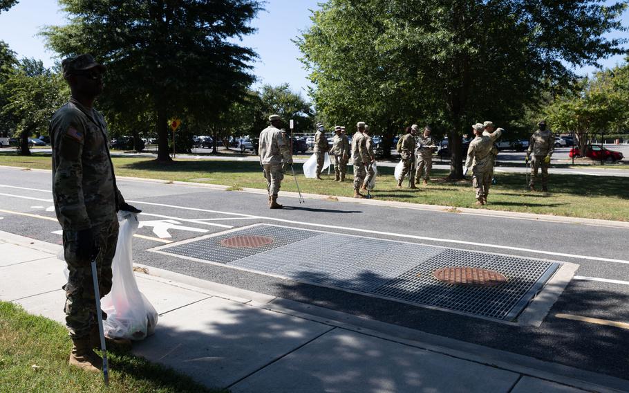 Soldiers walking across a street and onto a lawn, many of them with trash pickers.