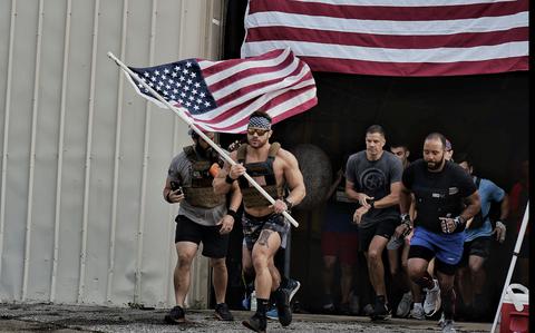 A group of mean, led by David Winne holding a flag, run out of a building that also has a giant flag on the front. 