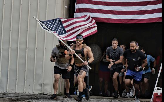 A group of mean, led by David Winne holding a flag, run out of a building that also has a giant flag on the front. 