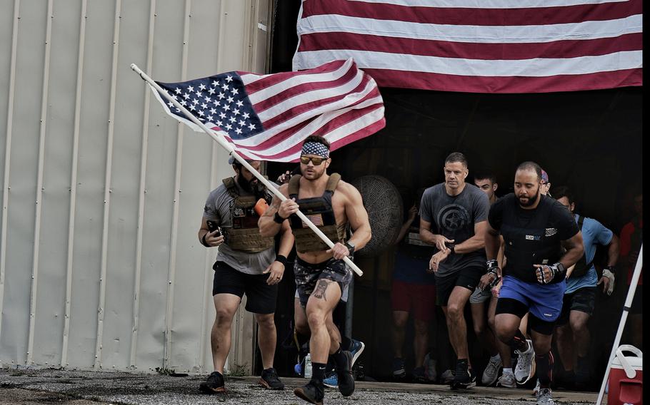 A group of men, led by David Winne holding a flag, run out of a building that also has a giant flag on the front. 